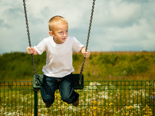 Little blonde boy child having fun on a swing outdoor