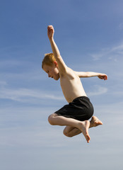 Fototapeta premium Young boy jumping in the air from sea wall at seaside.