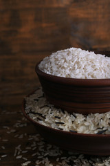 Grains of rice in bowls on wooden background