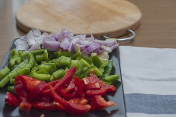 Sliced green and red peppers and onion on a wooden table