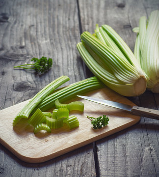 Fresh green celery stems on wooden cutting board closeup