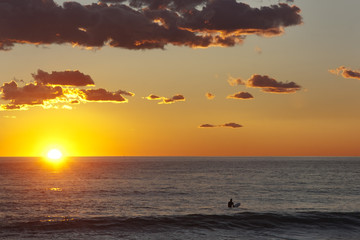 surfer in the water at sunset waiting for the last wave