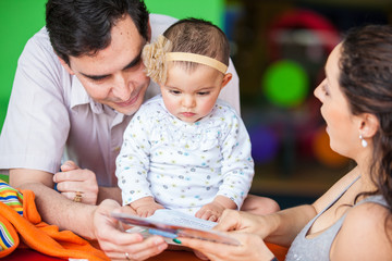 Padres jóvenes leyendo un cuento a su pequeña bebé de seis meses