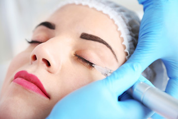 Cosmetologist applying permanent make up on eyes, close-up