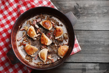 Fried dumplings with onion and bacon in frying pan,