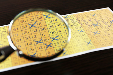 Analyzing lottery ticket with magnifier, closeup