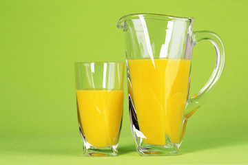 Glass and pitcher of orange juice on green background