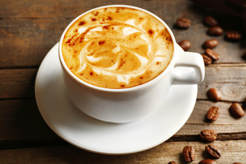 Cup of coffee latte art with grains on wooden table, closeup