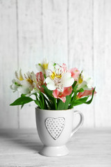 Fototapeta na wymiar Beautiful flowers in cup, on wooden background