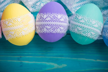 easter colored eggs with lace ribbon on blue wooden background