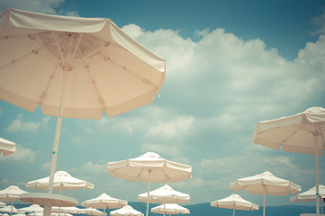 White sunshades on sea beach, cloudy sky in the background © AlvensAlv