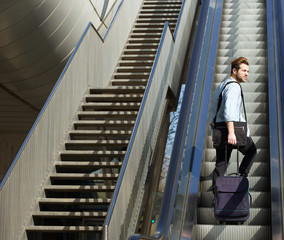 Handsome man walking up escalator with travel bags