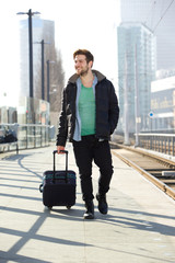 Young man smiling with suitcase on train station platform