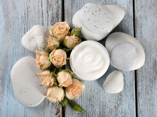 Cosmetic cream with flowers and spa stones on wooden background