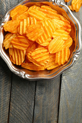 Delicious potato chips on plate on wooden table close-up