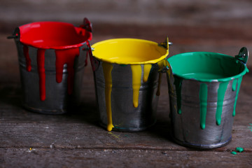 Metal buckets with colorful paint on wooden background