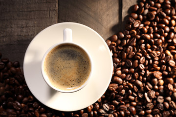 Cup of coffee with grains on wooden table, top view