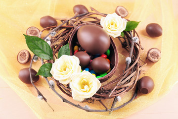 Chocolate Easter eggs with flowers in wicker nest, closeup