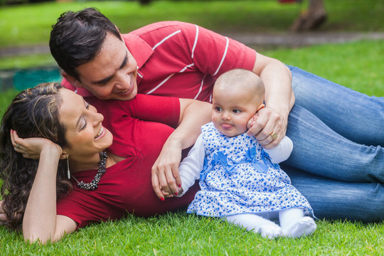 Pareja joven disfrutando de un hermoso d&iacute;a de sol con su bebita en un parque