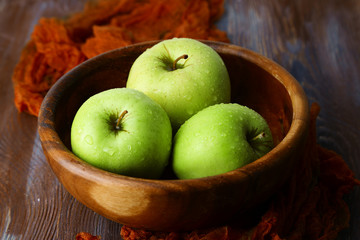 Green apples in bowl with fabric on wooden table, closeup