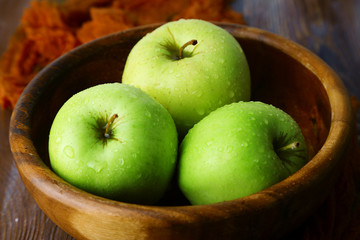 Green apples in bowl with fabric on wooden table, closeup