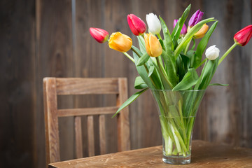 Coloful tulips in a vase on a wooden table