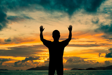 Fototapeta premium Silhouette man show two hands up in the air at sunset beach