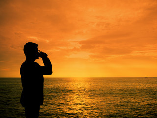 Silhouette man zipping coffee at sunset beach
