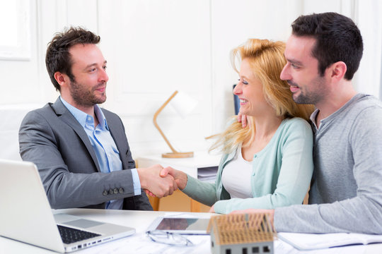 Young happy couple handshaking real estate agent after signing c