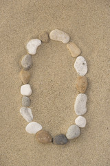 Fototapeta na wymiar Buchstabe O aus Kieselsteinen im Sand
