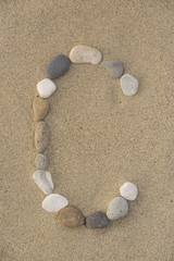 Fototapeta na wymiar Buchstabe C aus Kieselsteinen im Sand