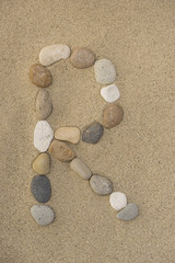 Fototapeta na wymiar Buchstabe R aus Kieselsteinen im Sand