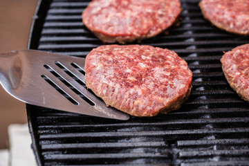 Grilled ground beef pattie burger on spatula against BBQ