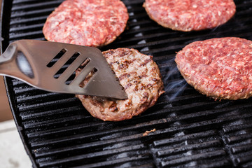 Grilled ground beef pattie burger on spatula against BBQ