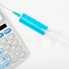 Calculator and a syringe with blue liquid inside - studio shot