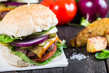  homemade burger with potato wegdes on wooden table