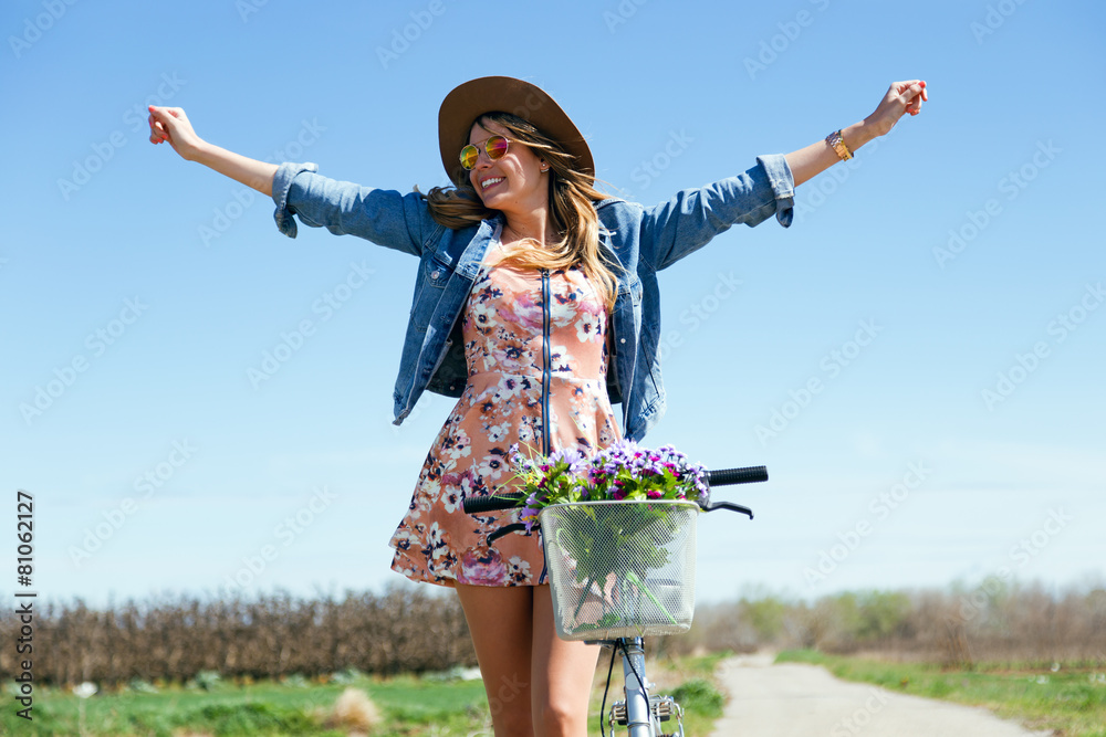 Wall mural beautiful young woman with a vintage bike in the field.