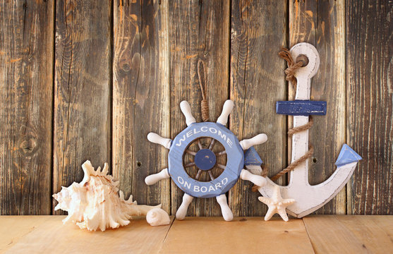 old nautical wood wheel, anchor and shells on wooden table over 