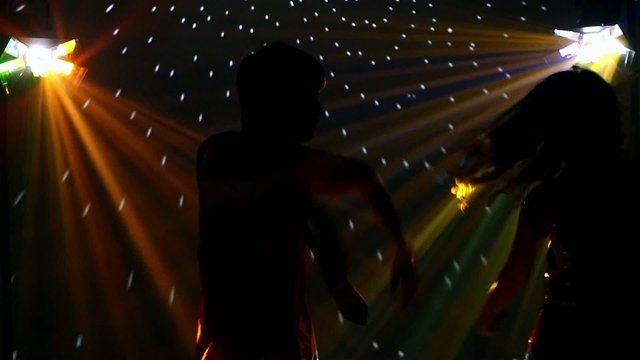 Girl and guy dancing in glow of LED spotlights. company friends