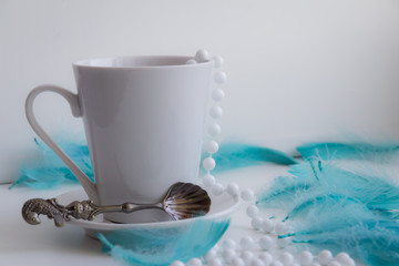 Still life with cup in white colors with cyan feathers