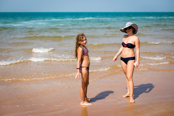 tanned woman and a girl standing on the beach