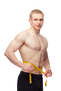 Fit man measuring his waist after a workout in the gym, isolated
