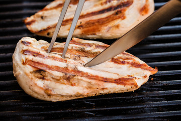 Grilled chicken breast fillets on BBQ with fork and knife