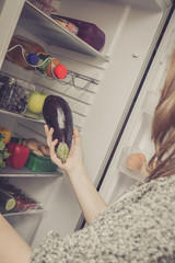 Junge Frau nimmt Obst und Gemüse aus dem Kühlschrank raus