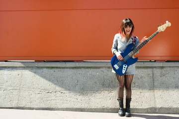 Laughing woman holding blue bass guitar outside