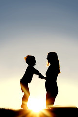 Fototapeta premium Silhouette of Mother and Young Child Holding Hands at Sunset