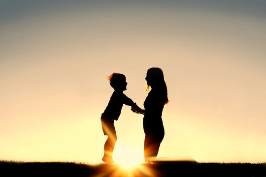 Silhouette of Mother and Young Child Holding Hands at Sunset