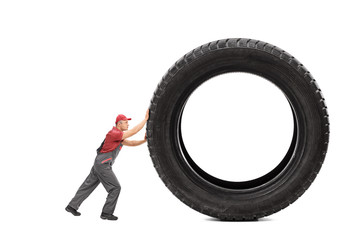 Mechanic in a gray jumpsuit pushing a giant black tire