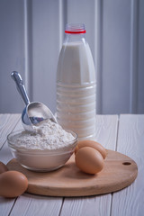 close up view eggs flour in bowl scoop bottle of milk on white p