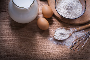 flour in bowl and spoon corolla egss pitcher with milk on wooden
